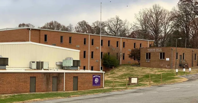 L'edificio in mattoni a più piani della Winston Salem Christian School con l'insegna lilla è circondato da alberi spogli.