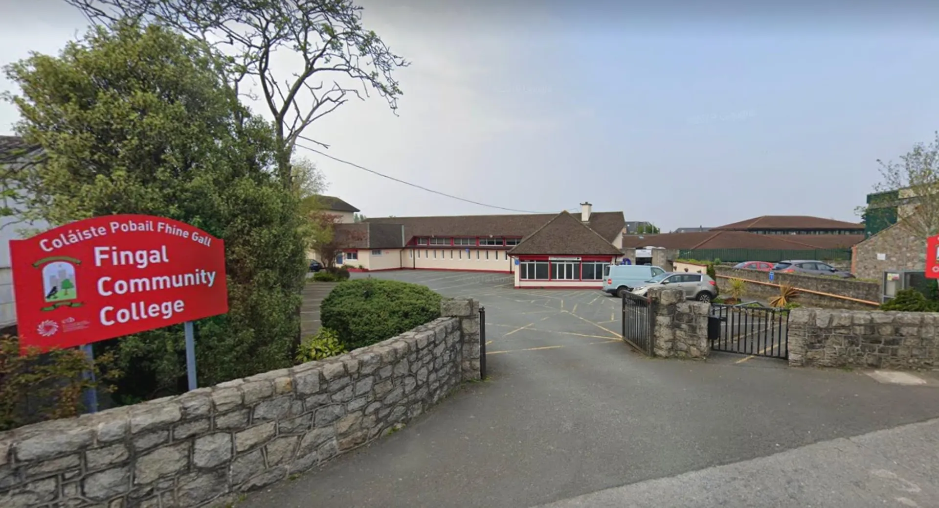 Un cartello rosso del Fingal Community College si trova davanti a un muro di pietra con edifici sullo sfondo.