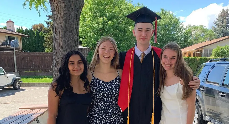 Un gruppo di studenti della Valleyview Secondary School insieme a un diplomato in toga all'aperto davanti ad alberi ed edifici.