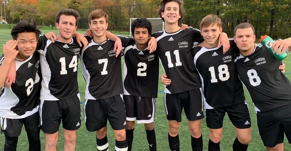 Un gruppo di studenti del Waterloo Catholic District School Board si trova su un campo sportivo circondato da alberi.