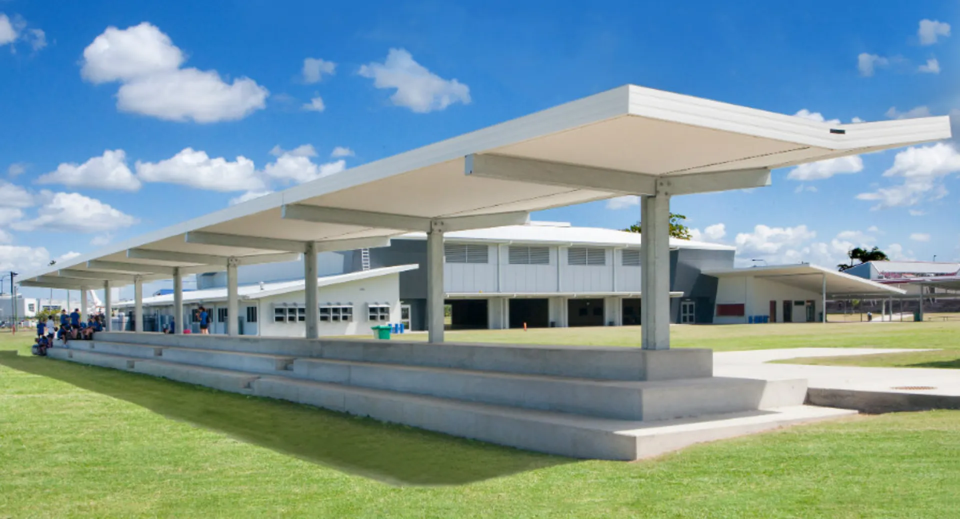 Il moderno edificio bianco della Hervey Bay State High School sorge su un prato sotto un cielo azzurro con nuvole bianche.