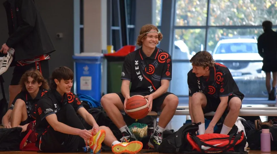 Studenti del Manea Senior College si preparano a un'attività sportiva in una stanza con un pallone da basket e vista sull'esterno.