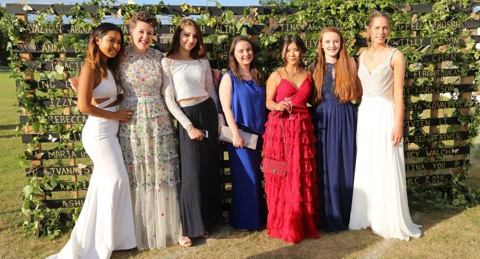 Un gruppo di giovani donne in abito formale sta davanti al giardino verde nel campus dell'Harrogate Ladies’ College.
