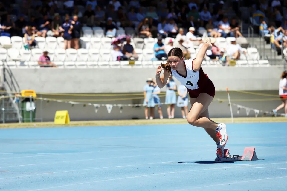 Un'atleta della St. Mary's Anglican Girls' School esegue un esercizio di ginnastica su un tappeto blu davanti al pubblico.