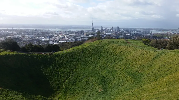 Grasbewachsener Vulkankrater mit Blick auf die Skyline von Auckland und den Sky Tower