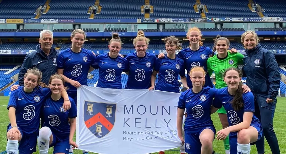Un gruppo di calciatrici della Mount Kelly School posa insieme con uno striscione sul campo da gioco.