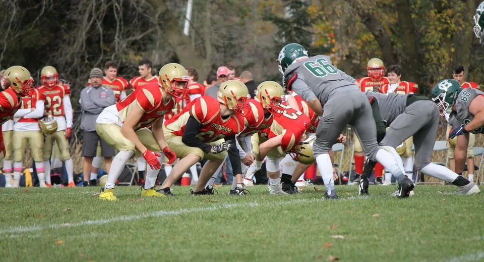 Studenti della Sydenham High School giocano una partita di football sul campo davanti a uno sfondo di bosco autunnale.
