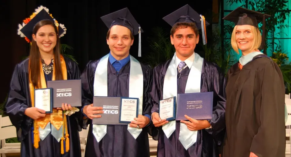 Quattro diplomati in toga nel campus del Beech Hill College tengono in mano i loro diplomi all'aperto.