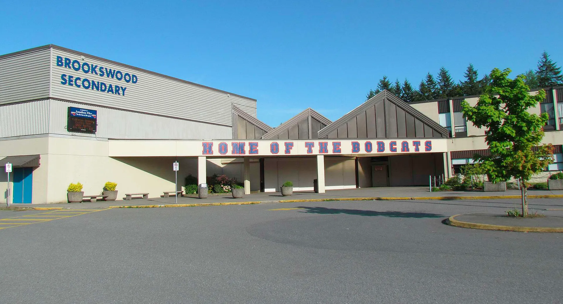 L'edificio scolastico moderno della Brookswood Secondary School è circondato da alberi e si trova accanto a un parcheggio pavimentato.