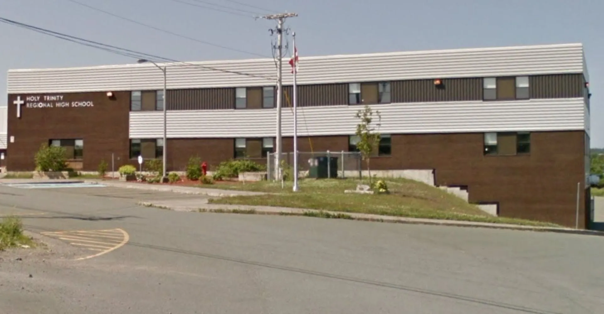 L'edificio a più piani della Holy Trinity High School con facciata marrone si trova circondato da un'area verde e una strada in primo piano.