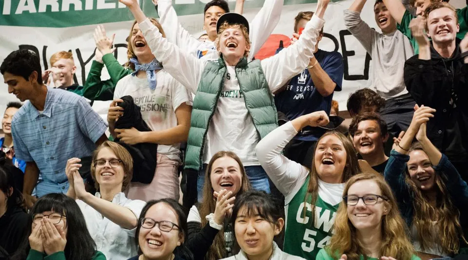 Un grande gruppo di studenti della Charles Wright Academy festeggia insieme a braccia alzate all'interno di uno spazio al chiuso.