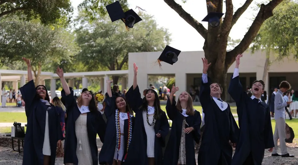 Studenti diplomati della Trinity Preparatory School lanciano in aria i tocchi indossando le toghe blu.