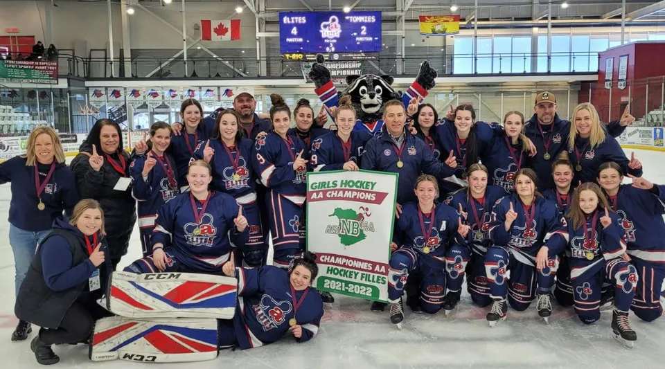 La squadra femminile di hockey su ghiaccio della Polyvalente Thomas-Albert si trova nel palazzetto del ghiaccio con le sue maglie blu davanti alla bandiera canadese e britannica.