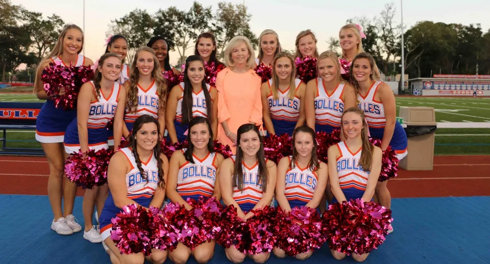 Un gruppo di cheerleader della The Bolles School è insieme sul campo sportivo con divise uniformi e pompon.