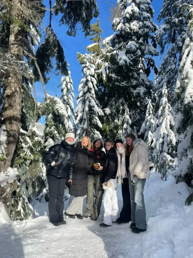 Gruppo di studentesse in giacca invernale tra abeti innevati in Canada