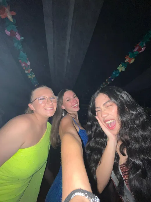 Tre ragazze sorridenti si fanno un selfie a una festa serale con ghirlande di fiori