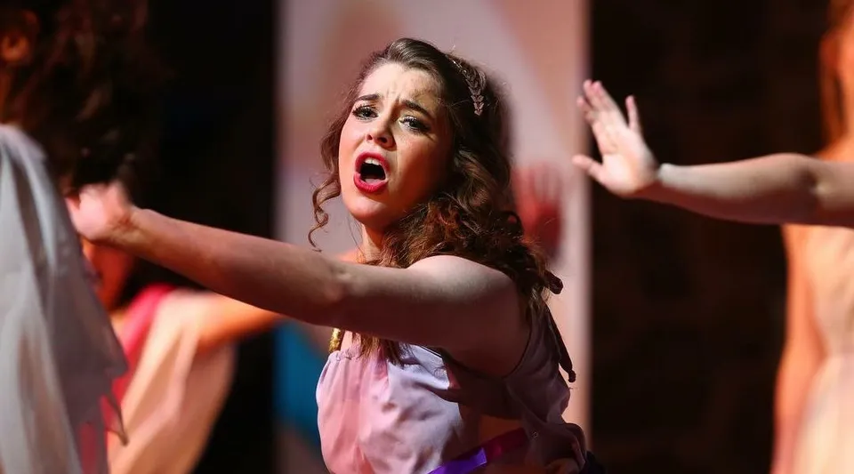 Una studentessa della Covenant Christian High School canta sul palco davanti a uno sfondo colorato.