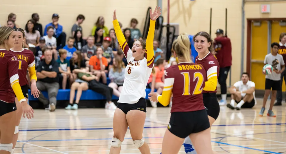 Studentesse della Three Hills School giocano a pallavolo sul campo all'aperto con spettatori sullo sfondo.