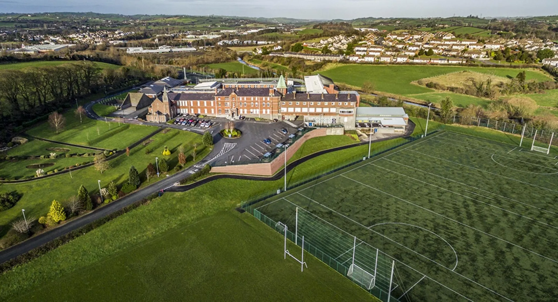 L'edificio principale del St. Colmans College si trova su una collina erbosa con case residenziali e molto verde sullo sfondo.