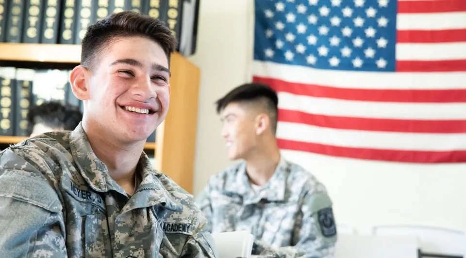 Due militari sorridenti in uniforme si trovano davanti alla bandiera americana nel terreno della Army and Navy Academy.
