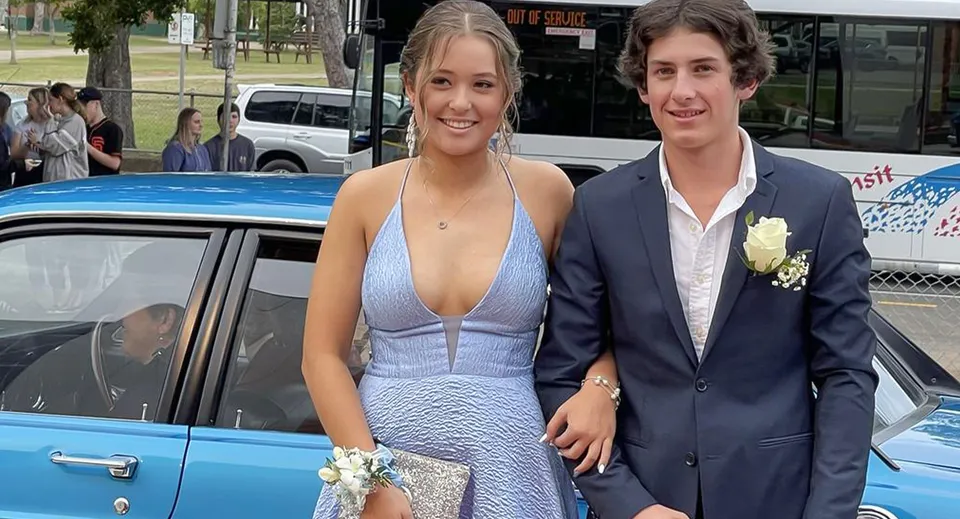 Una giovane coppia sta davanti a un'auto blu di fronte alla Maryborough State High School.