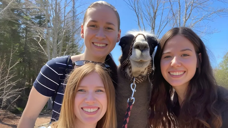Tre donne sorridenti posano con un grande cane nel bosco sul terreno della École L’Odyssée.