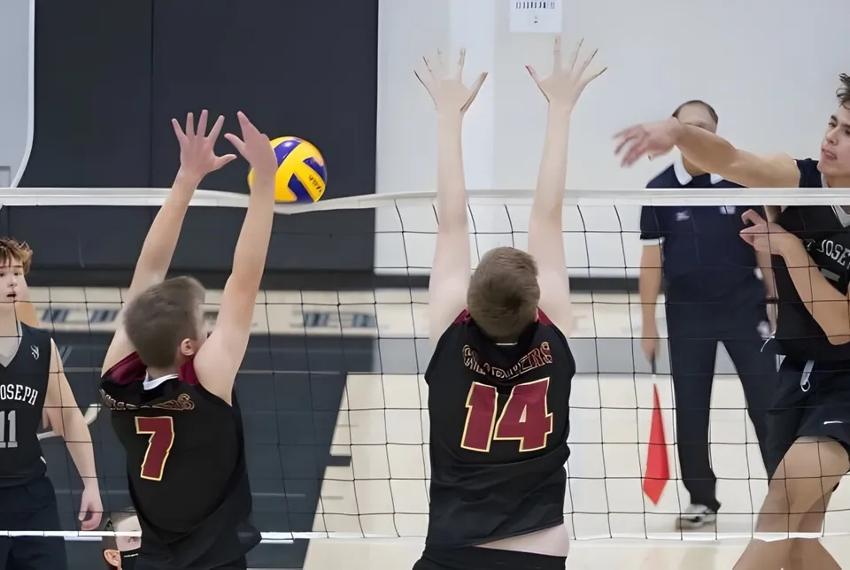Studenti e studentesse della St. Joseph High School giocano a pallavolo e cercano di murare il pallone a rete.