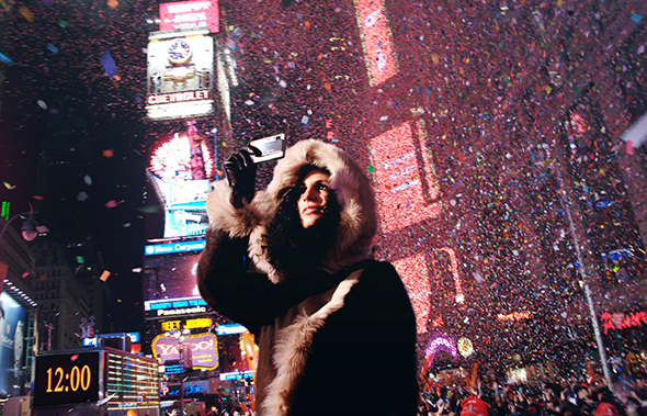 Una mujer con abrigo de capucha hace una foto en Times Square rodeada de confeti