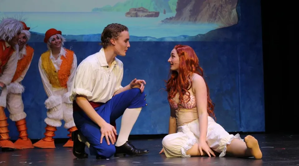 Spettacolo teatrale che mostra una coppia sul palco davanti a una scenografia con un paesaggio oceanico nel campus della The Vanguard School.