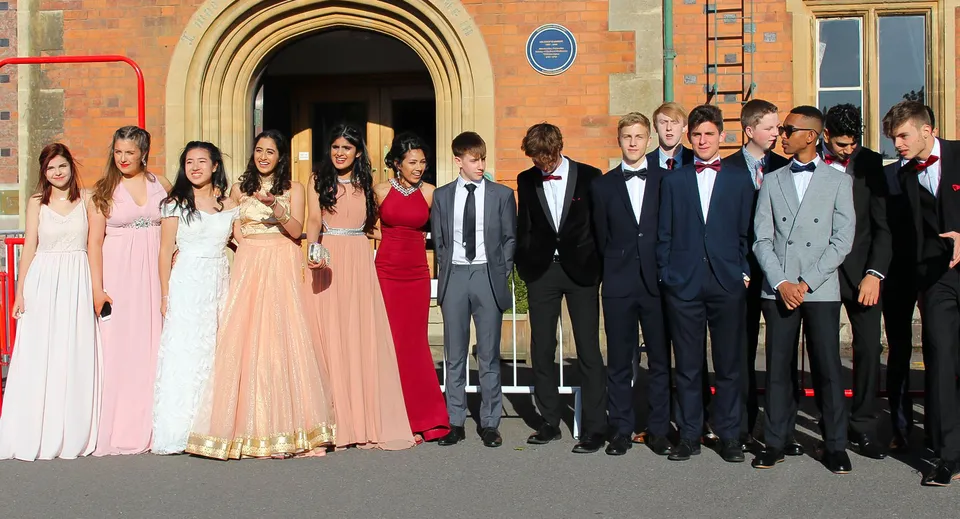Un gruppo di persone vestite in modo formale posa davanti a un arco decorato nel campus della The Royal School Wolverhampton.