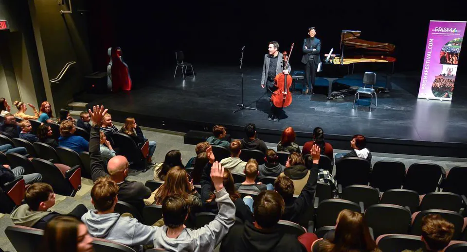 Un violoncellista e un pianista della Brooks Secondary School si esibiscono su un palco davanti a un pubblico seduto.