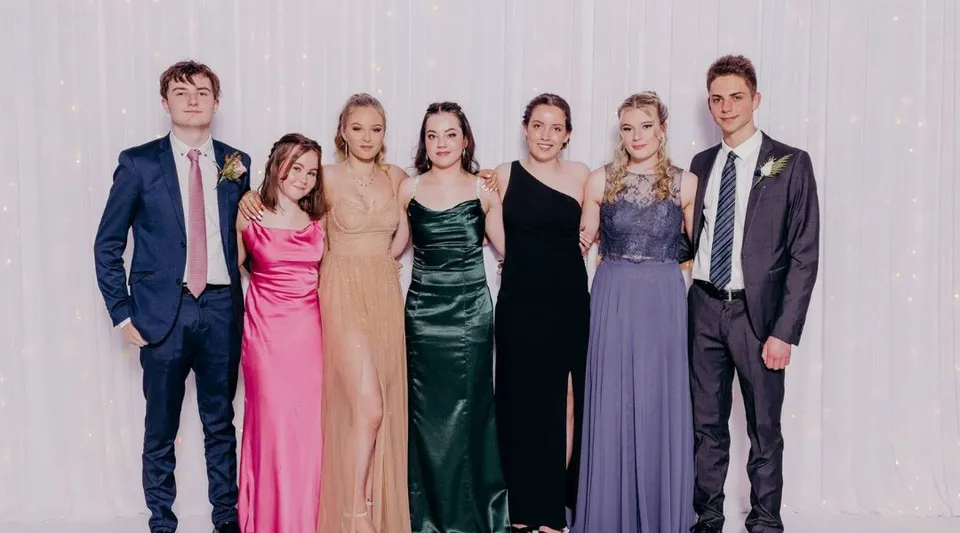 Un gruppo di sei persone in abbigliamento formale posa davanti a uno sfondo neutro al Kaikorai Valley College.