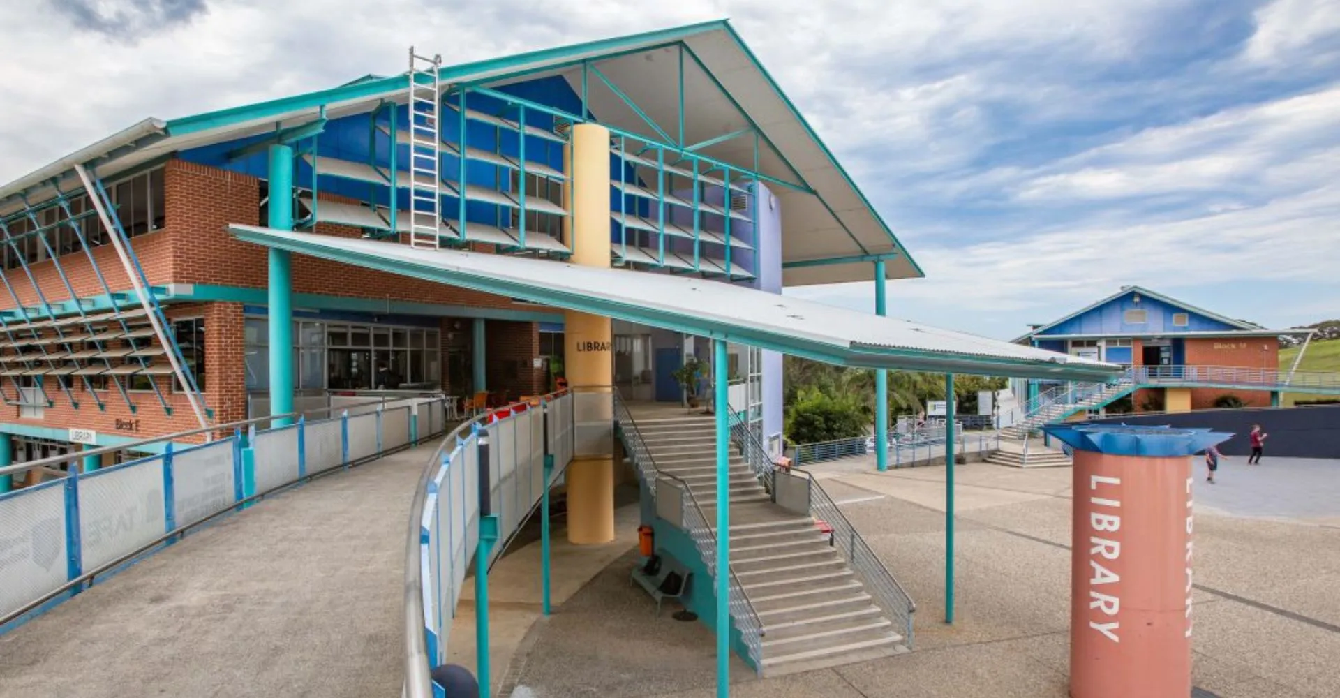 L'edificio moderno con ingresso e scalinata del Coffs Harbour Senior College sotto un cielo nuvoloso.
