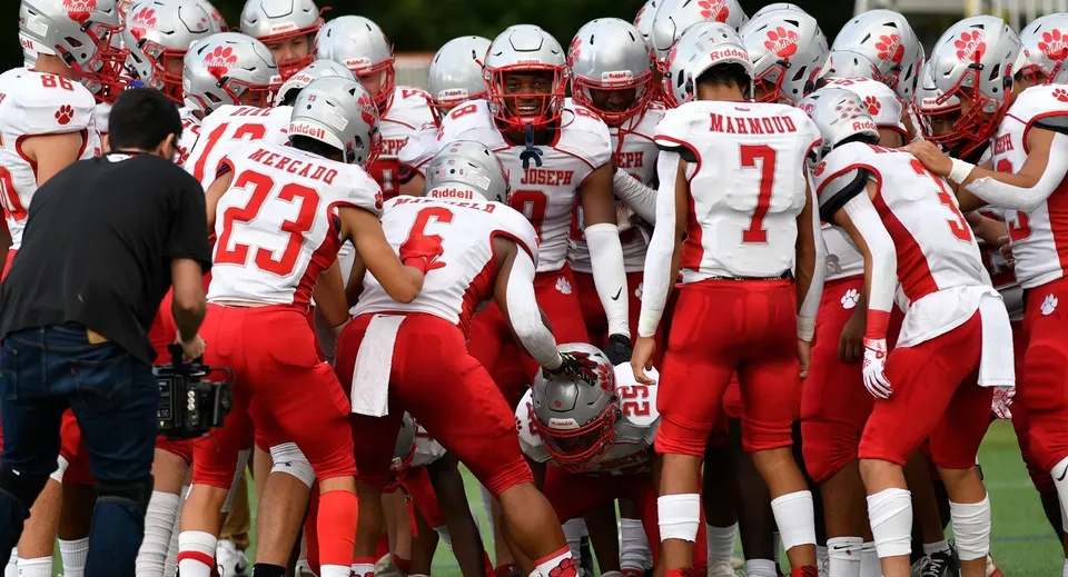 I giocatori di football americano della St. Joseph High School si radunano sul campo in divisa rossa e bianca.