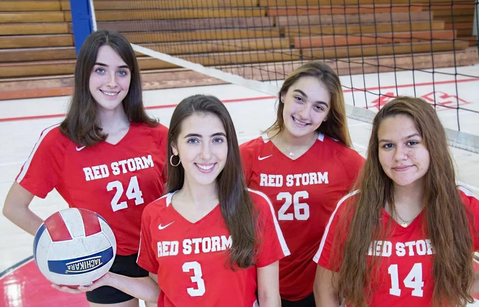 Quattro studentesse della Saint Johns High School indossano maglie rosse con la scritta Red Storm e si trovano insieme in una palestra.
