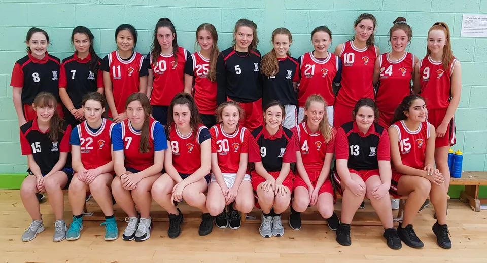 Un gruppo di giovani giocatrici di pallavolo in maglia rossa e nera sul campo della Scoil Mhuire (Trim).