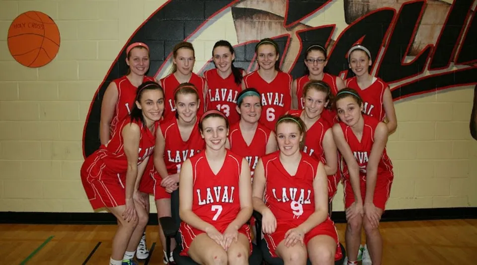 Un gruppo di giovani studentesse della Laval High School in uniforme rossa posa nella palestra davanti a un grande murale dedicato al basket.