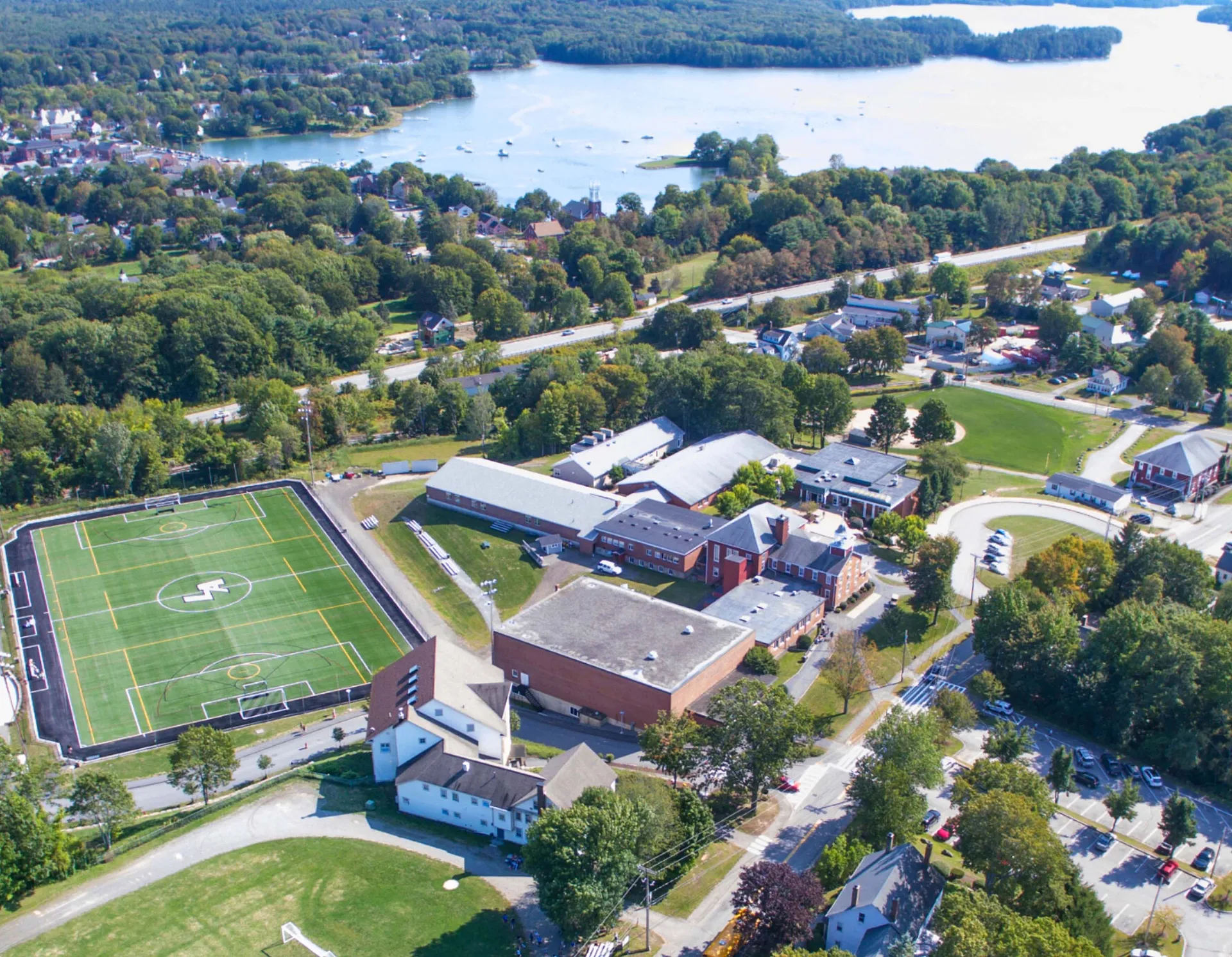 Vista aerea della Lincoln Academy con campo sportivo ed edifici circondati da verdi boschi.