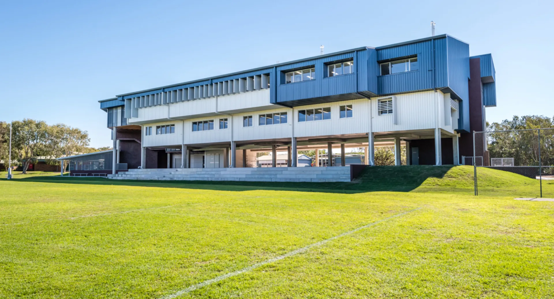 L'edificio moderno a più piani della Castlerea Community School sorge su un prato circondato da alberi sotto un cielo azzurro.