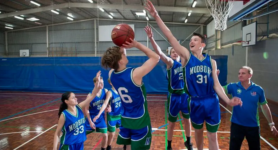Un gruppo di giocatori di basket della Modbury High School si sfida sul campo, mentre un giocatore blocca un tiro.
