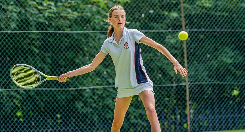 Una studentessa della Godolphin School colpisce una pallina da tennis con la racchetta.