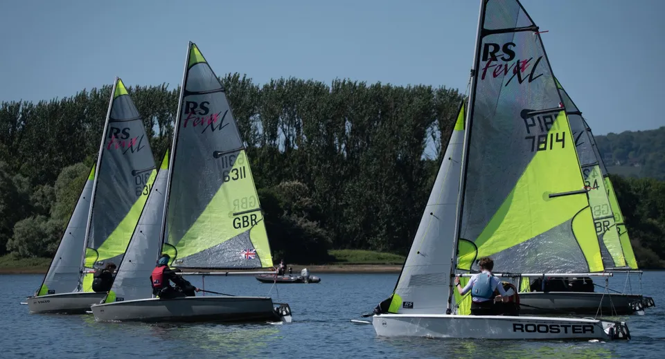 Barche a vela scivolano su uno specchio d'acqua calmo davanti a un paesaggio verde nel campus del Cardiff Sixth Form College.