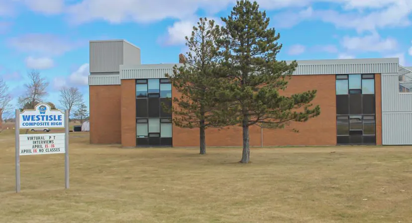 L'edificio moderno a più piani della Westisle Composite High School con un grande pino in primo piano sotto un cielo blu.