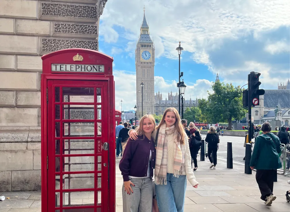 Zwei Mädchen in London vor einer roten Telefonzelle, mit Big Ben im Hintergrund.