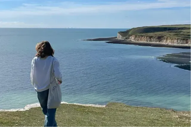 Studentessa di spalle osserva il mare e le bianche scogliere lungo la costa