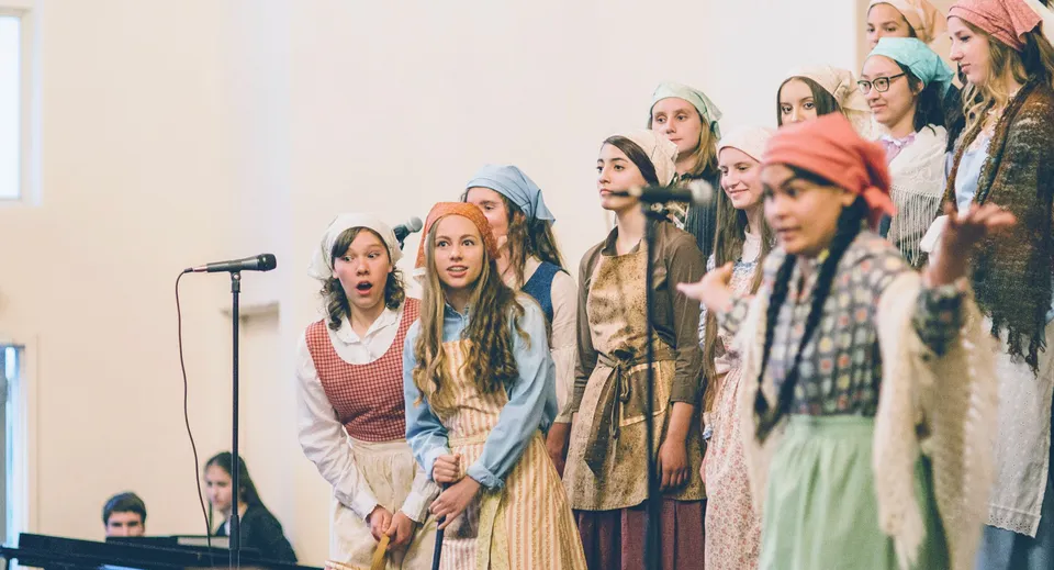Un gruppo di giovani donne si trova con i microfoni sul palco della Covenant High School durante un'esibizione.