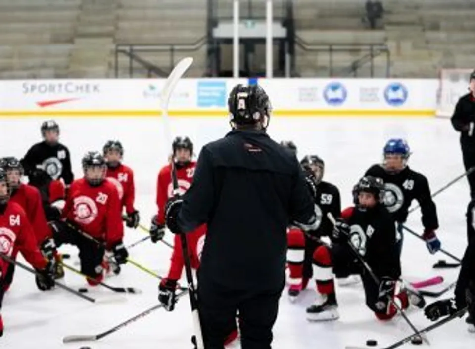 Un allenatore di hockey si rivolge a giovani giocatori sul ghiaccio alla Ottawa Sports Academy Private School.