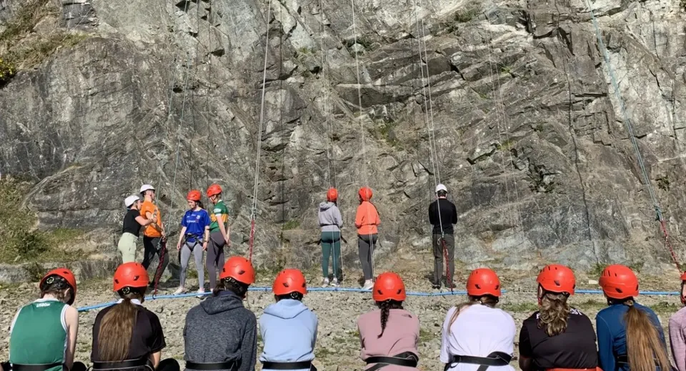 Studentesse del Our Lady's College con caschi e imbragature davanti a una parete di roccia.