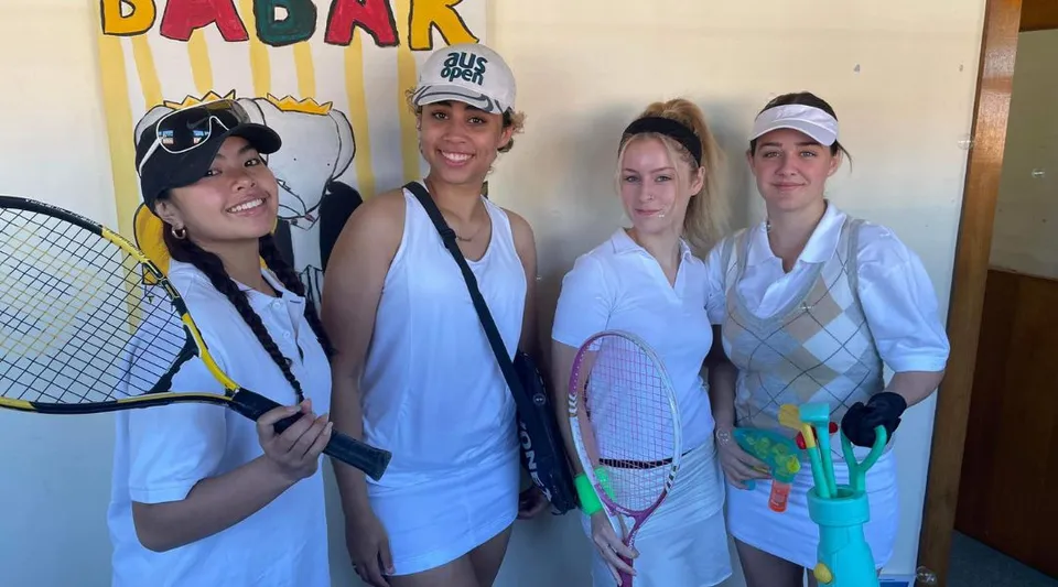Quattro studentesse della Port Hacking High School posano insieme davanti al variopinto cartello Badark.