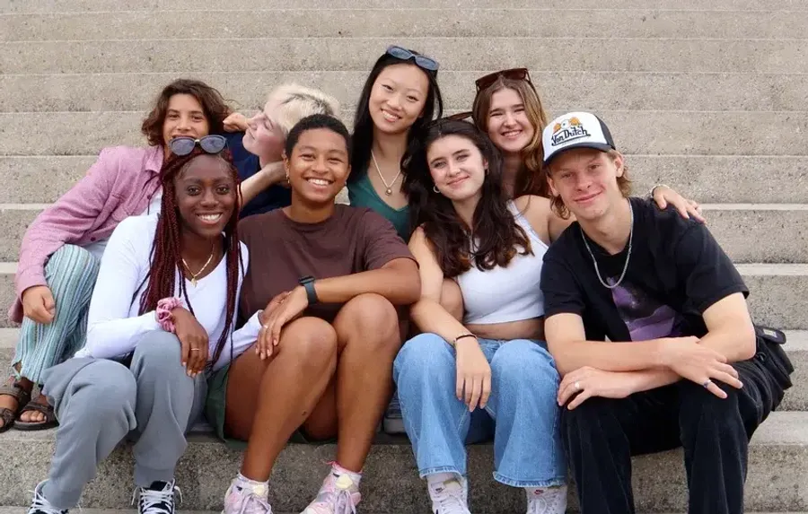 Gruppo di ragazzi sorridenti seduti insieme su una scalinata durante un soggiorno studio